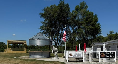 Rural Texas property with large water tank, American flag, and white fence gate with live bait shop sign