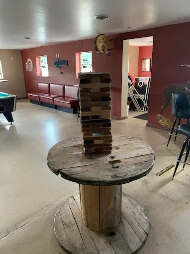 A tall wooden Jenga tower stacked on a round table in a recreation room with red walls and burgundy seating