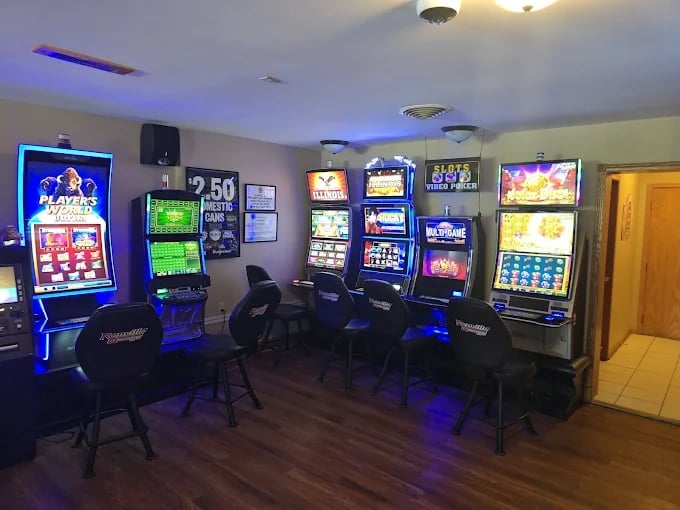 A game room with multiple slot machines and arcade games lit with blue ambient lighting and neon signs
