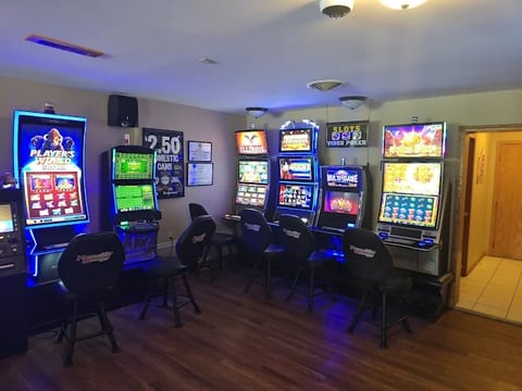 A game room with multiple slot machines and arcade games lit with blue ambient lighting and neon signs